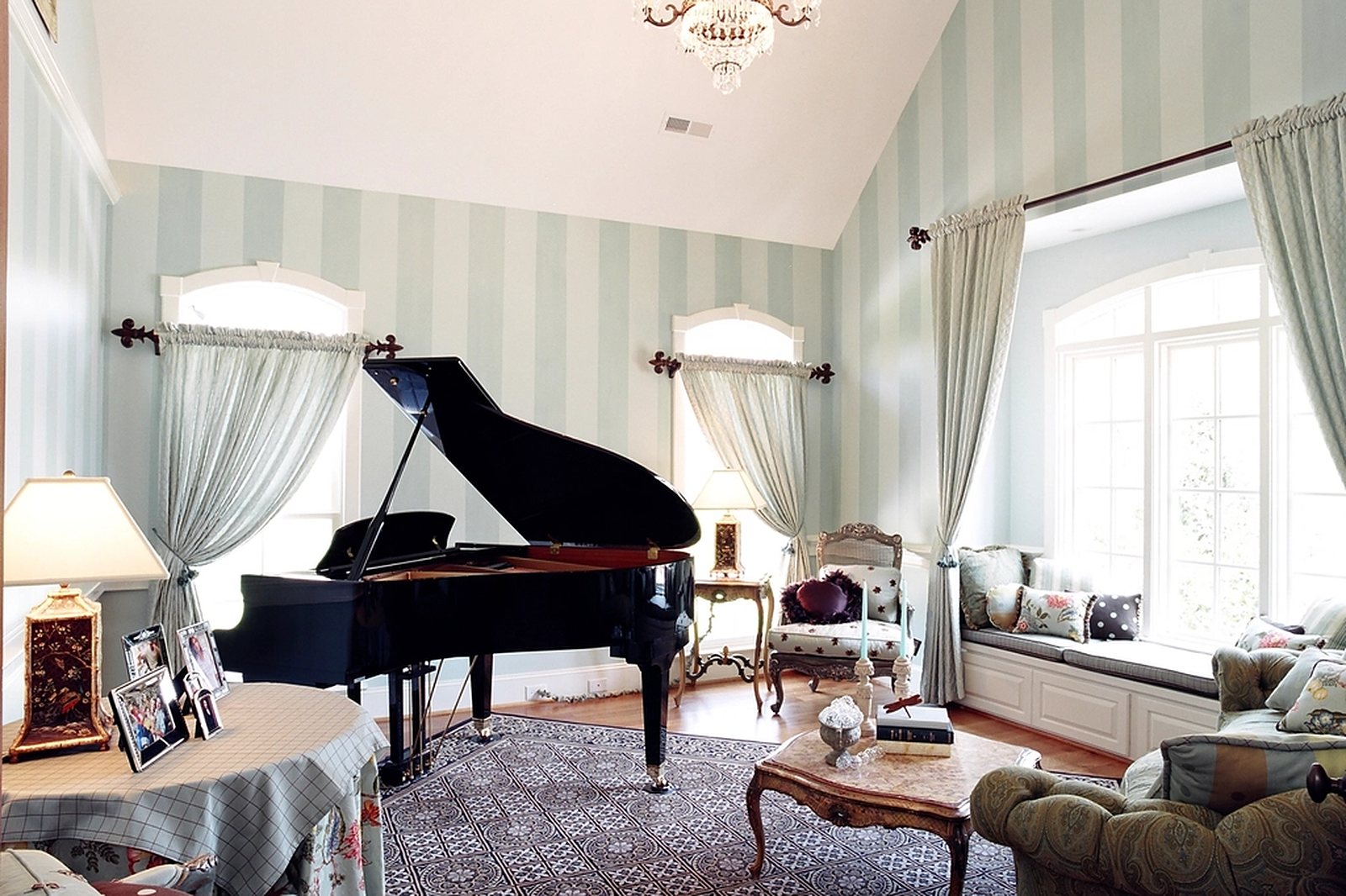 Elegant residential parlor with softly striped wallpaper, a grand piano and a bright window seat